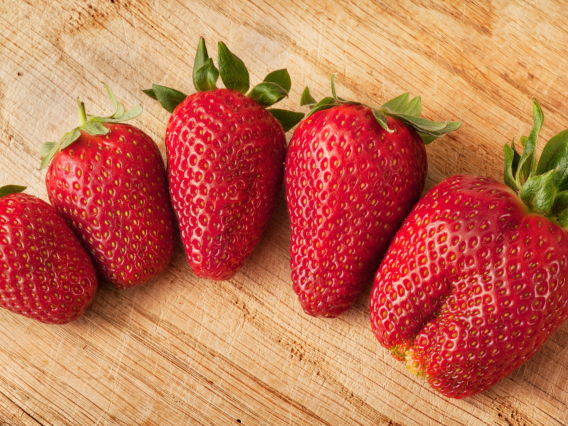 Five strawberries of different sizes and shapes arranged on a brown table.